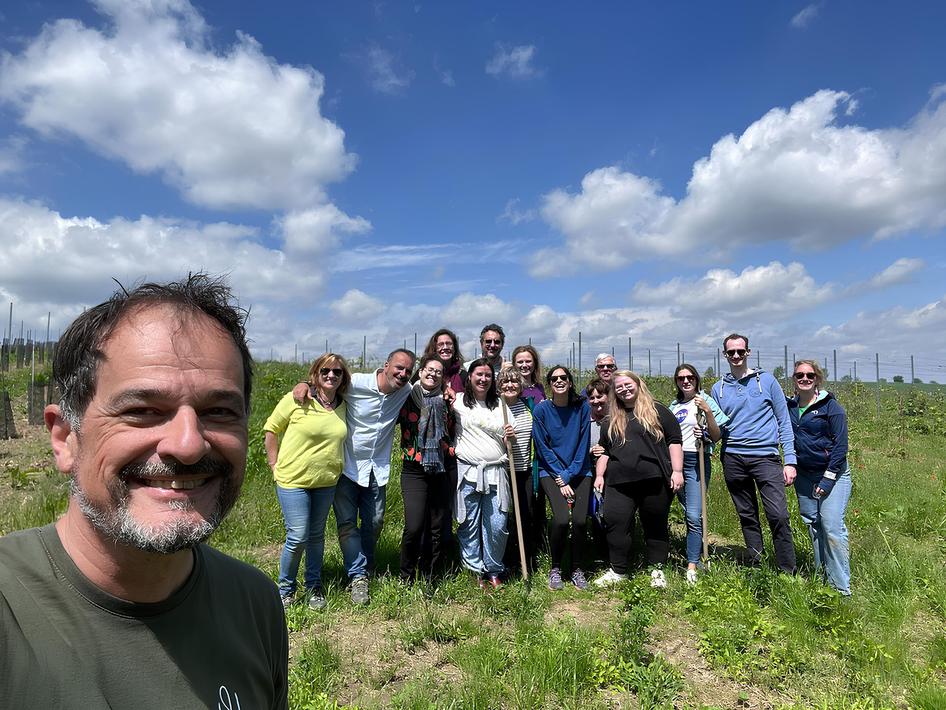 Denis et un groupe de volontaires souriants posent ensemble dans un vignoble, manifestant un esprit de convivialité et de collaboration, avec des rangs de vignes en arrière-plan.