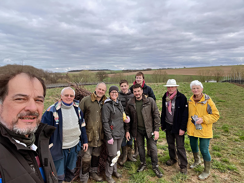 Un groupe de bénévoles et de membres du vignoble pose ensemble dans un champ, souriant après une séance de travail, sous un ciel nuageux