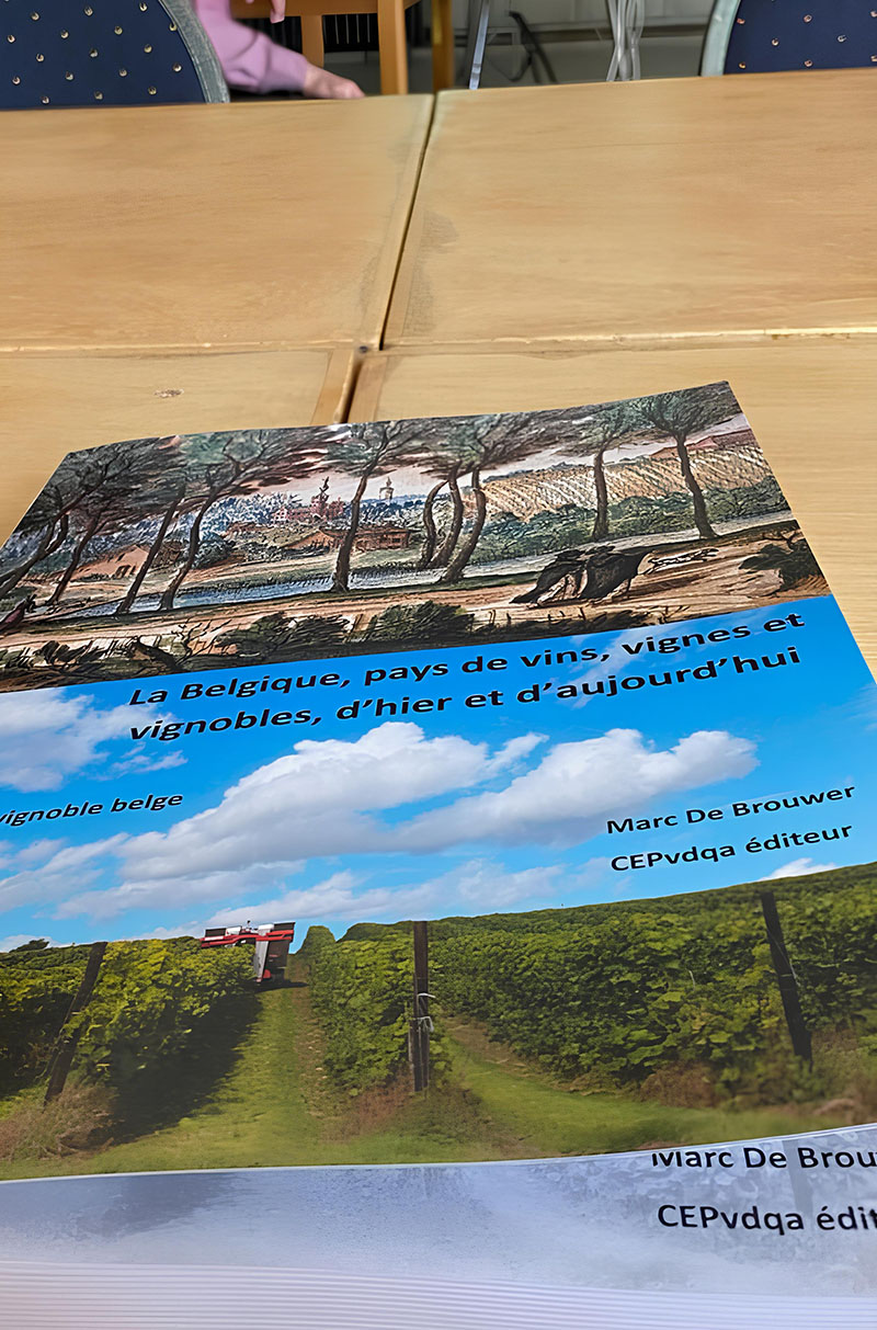 Un livre intitulé "La Belgique, pays de vins, vignes et vignobles, d'hier et d'aujourd'hui" de Marc De Brouwer est posé sur une table, avec sa couverture représentant des paysages viticoles belges.