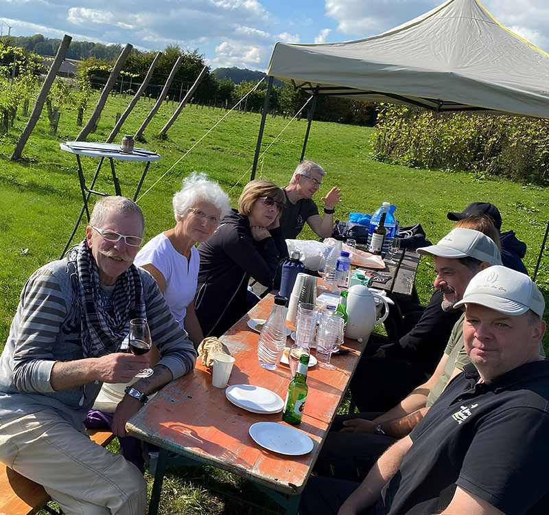 Groupe de personnes assises autour d’une table en plein air, dégustant du vin et partageant un repas dans le vignoble.